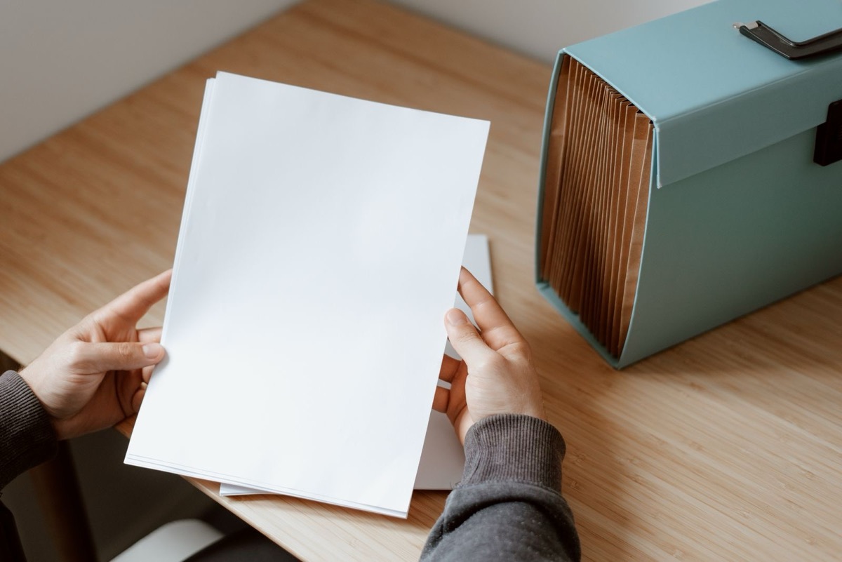 Hands holding blank sheets at a desk beside a file box