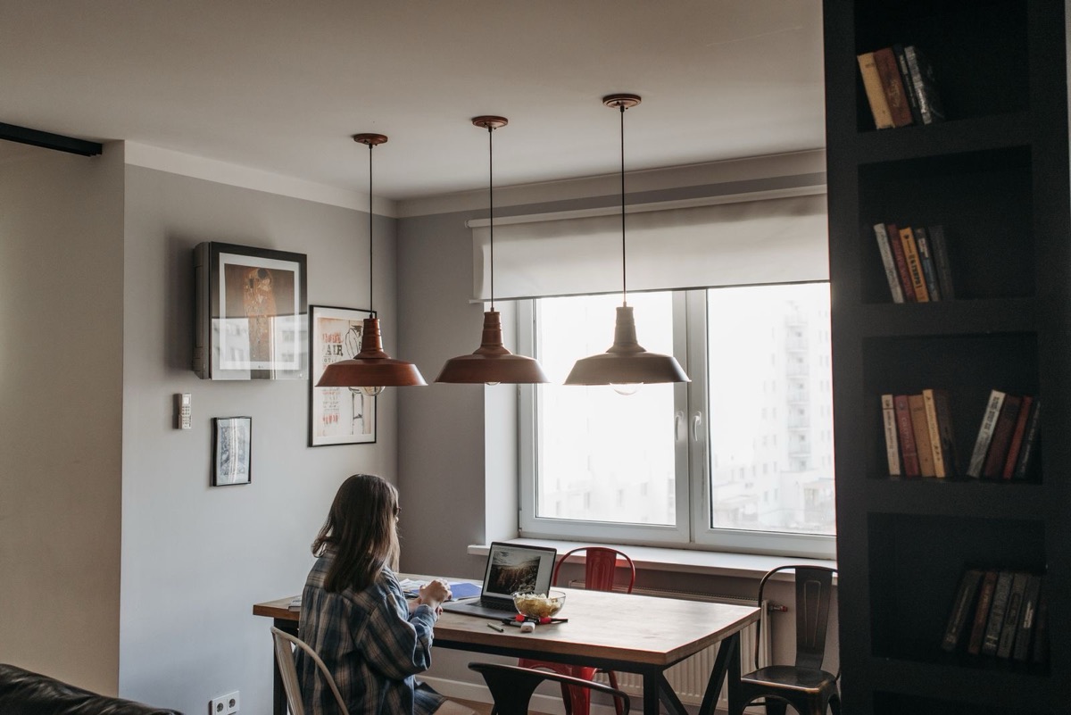 A person seen from behind working at a laptop at a dining table