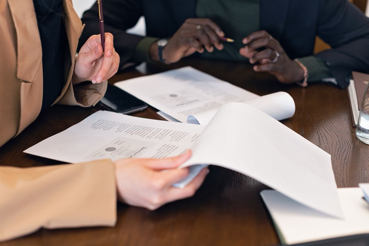 Hands turning printed pages at a wooden meeting table