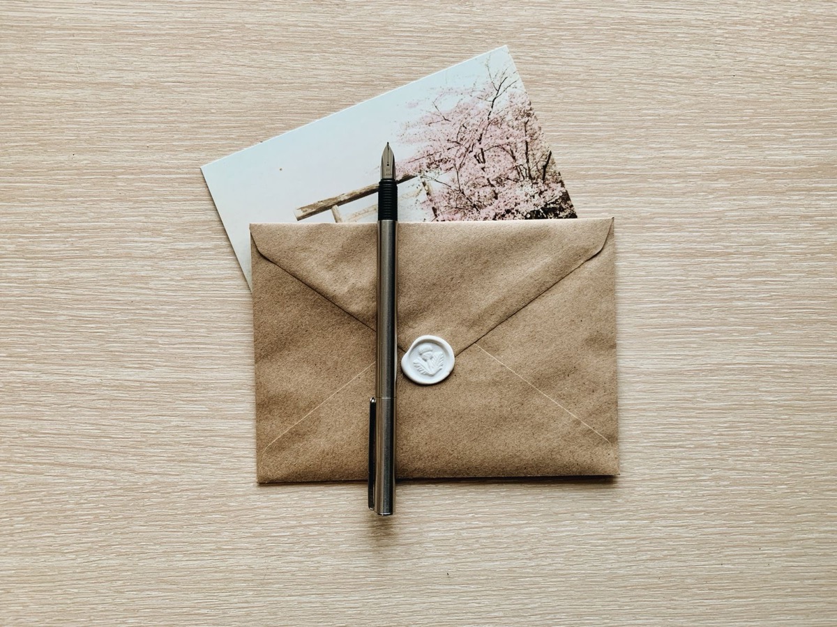 A kraft envelope closed with a white wax seal, a pen laid across it
