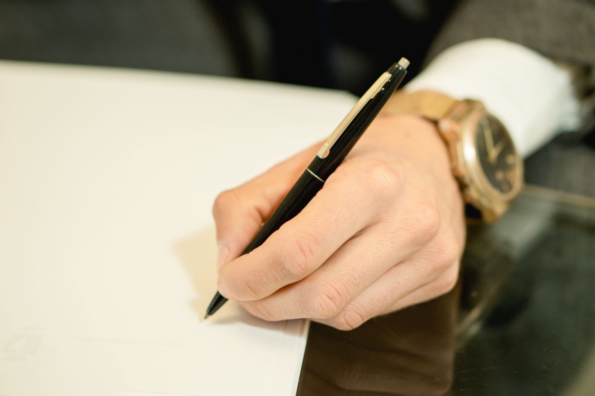 A hand writing with a pen on a blank sheet