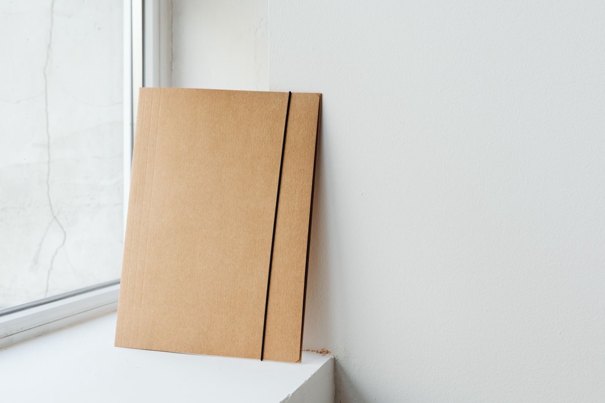 A kraft card folder with an elastic band standing by a window