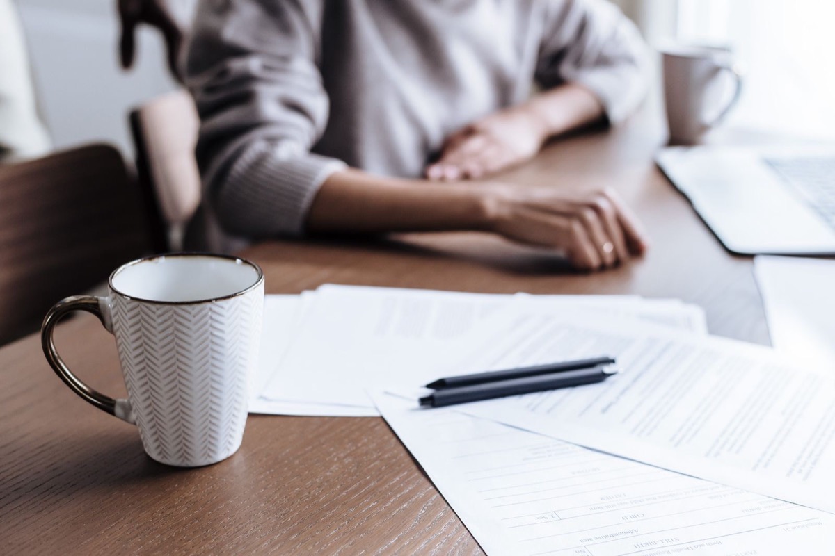 A pen resting on printed pages beside a coffee cup on a wooden desk