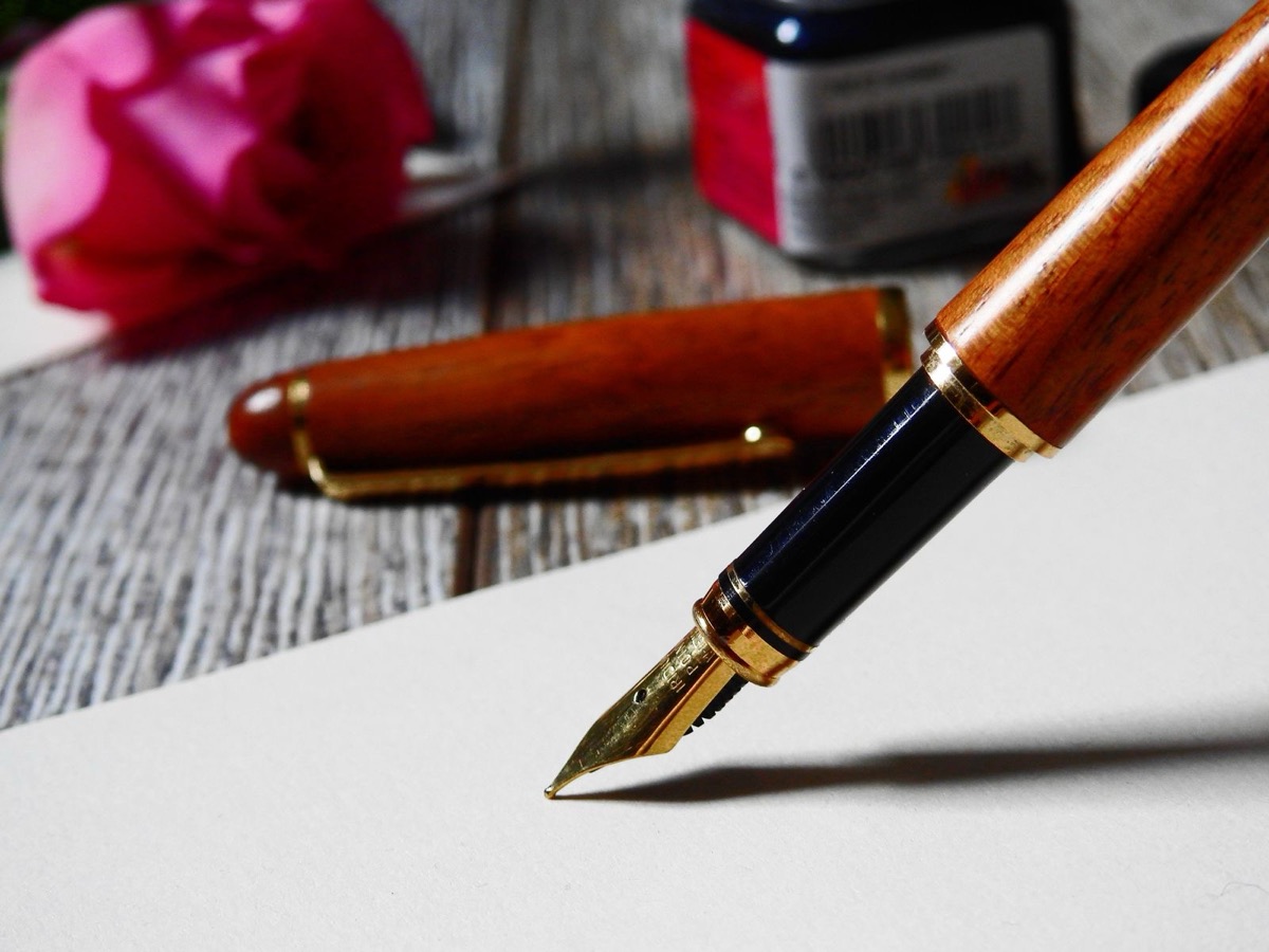 A fountain pen over a blank sheet beside its cap and an ink bottle