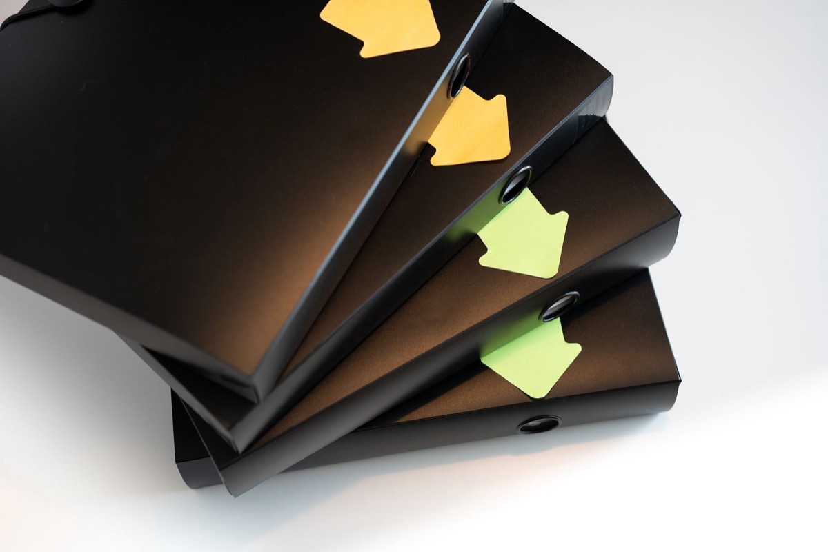 Four black ring binders fanned out, with yellow and green arrow tabs