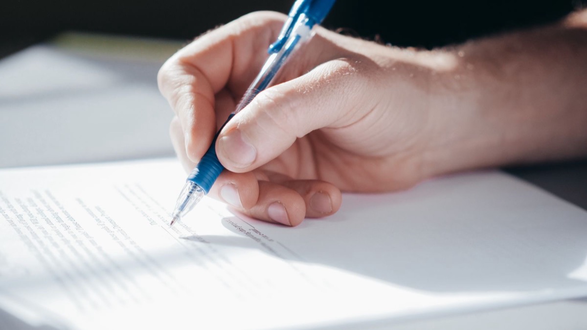 A hand signing a printed page with a ballpoint pen