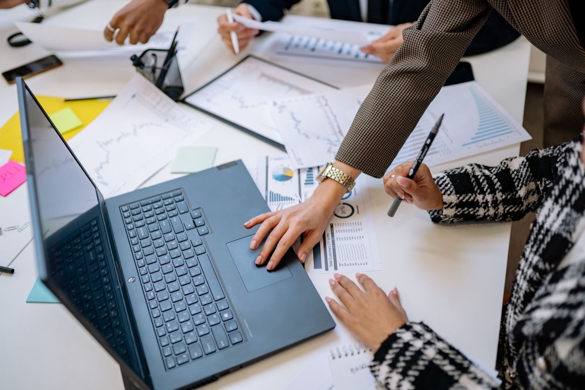 Hands at a laptop and printed charts on a shared meeting table