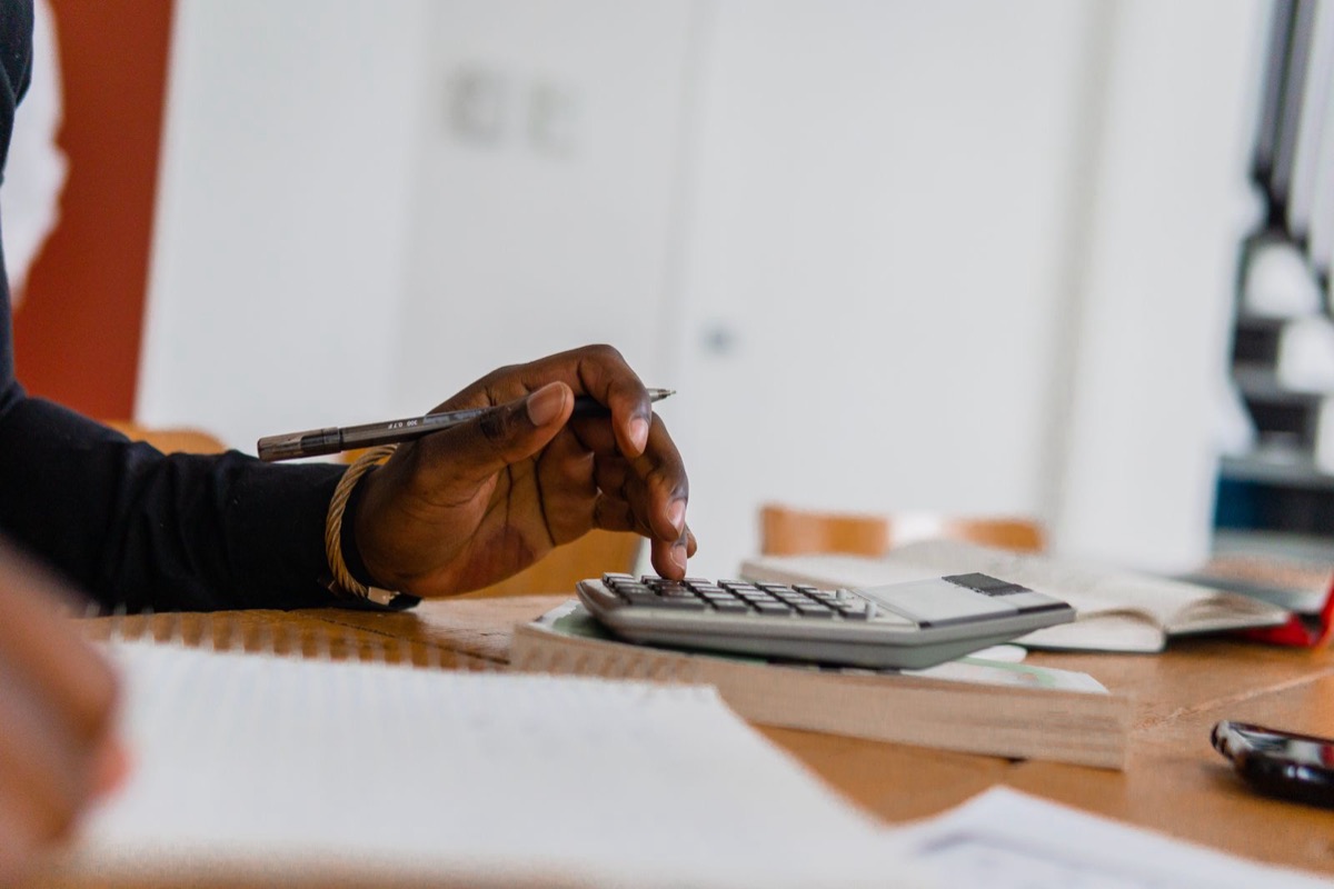 A hand with a pen using a calculator at a desk